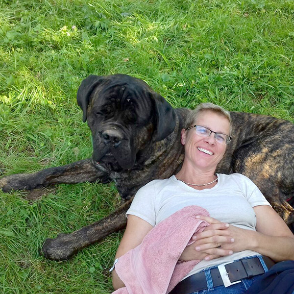 Karin Miller liegt im Gras mit dem Kopf auf Hund Antons Bauch.