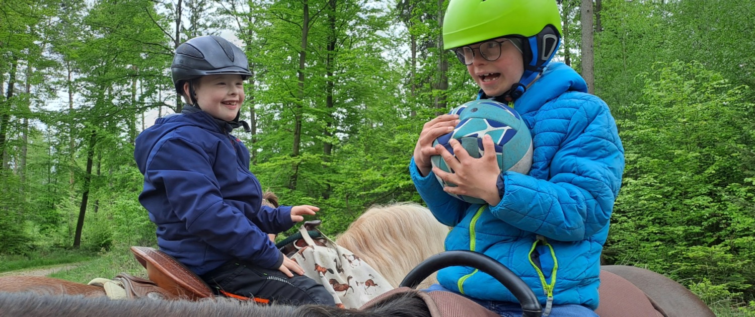 Im Wald auf Pferden sitzend spielen zwei Jungen Ball