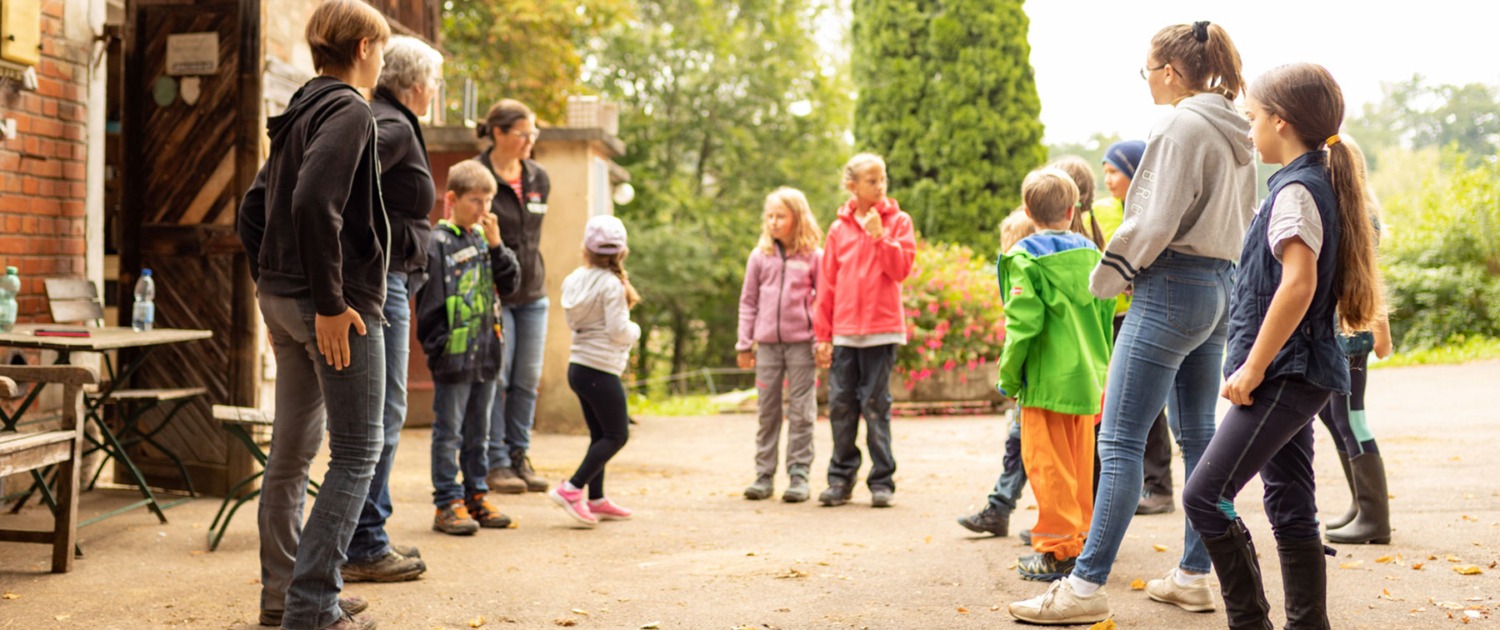 Eine Gruppe von Kindern und Erwachsenen stehen zu einer Besprechung im Kreis